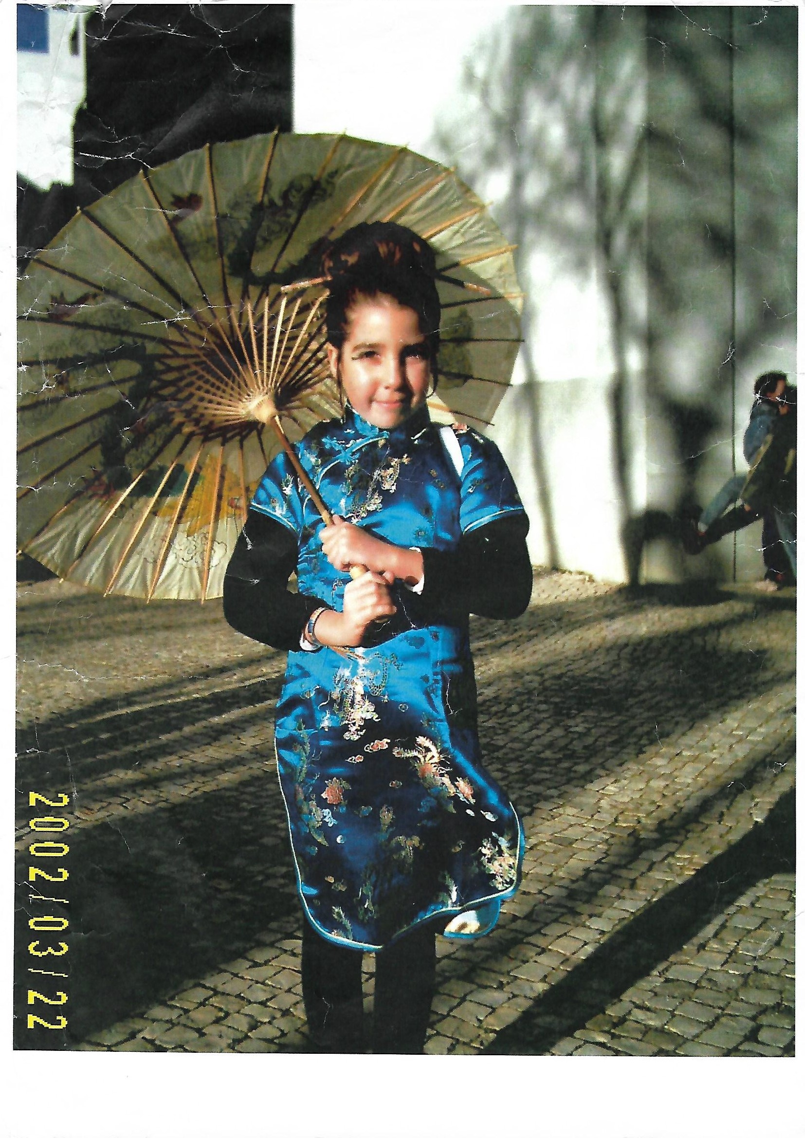 Inês as a little girl in a blue dress holding a paper parasol, 2002